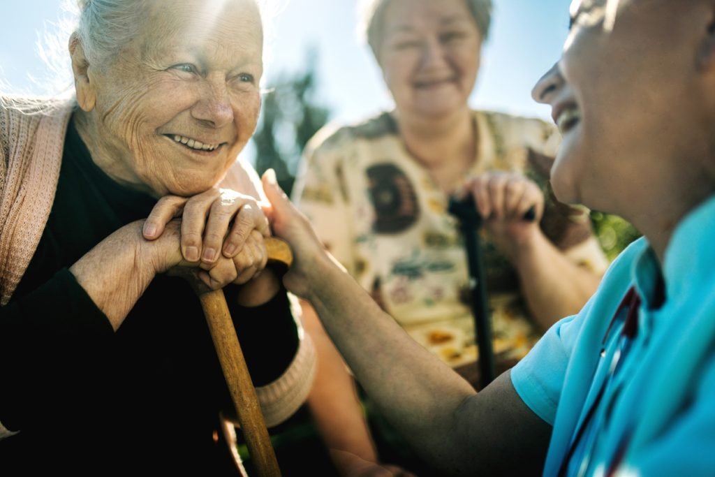 Elderly senior woman on wheelchair with a nurse outdoor in nursing hospital garden